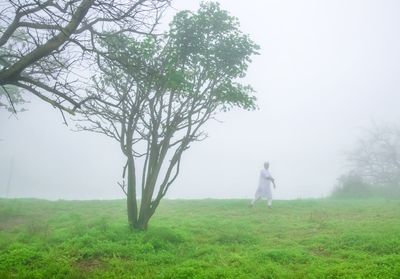 Man standing by tree on field against sky