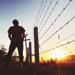 Rear view of silhouette man standing on field against sky during sunset