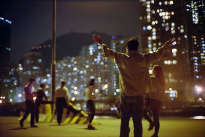 Rear view of man with arms raised in city at night