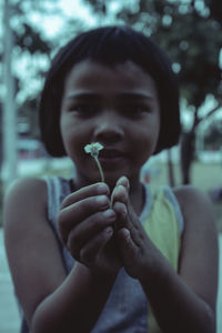 Portrait of cute girl holding flower while standing outdoors