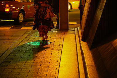Low section of woman walking on illuminated street at night