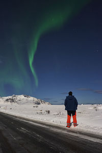 Rear view of man standing on snow at night