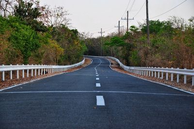 Empty road amidst trees against sky