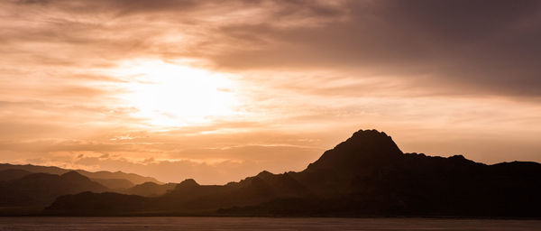 Silhouette mountain by sea against sky during sunset