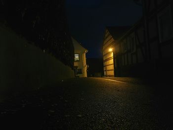 Illuminated road amidst buildings against sky at night