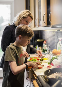 Son and mother cutting vegetables in kitchen