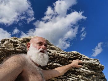 Low angle view of man sitting on rock against blue sky