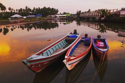 Boats moored in lake against sky during sunset