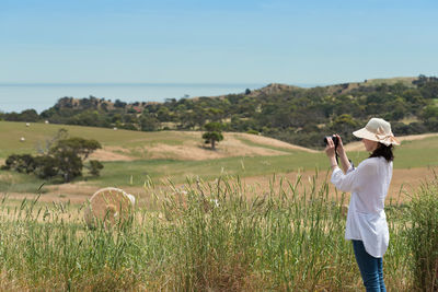 Side view of woman photographing on grassy hill