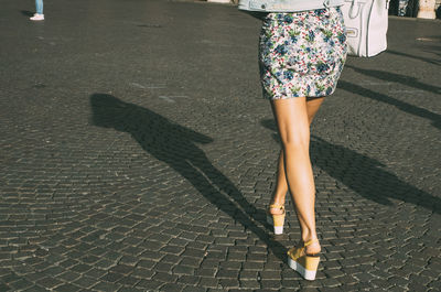 Low section of fashionable woman wearing sandals while walking on cobblestone