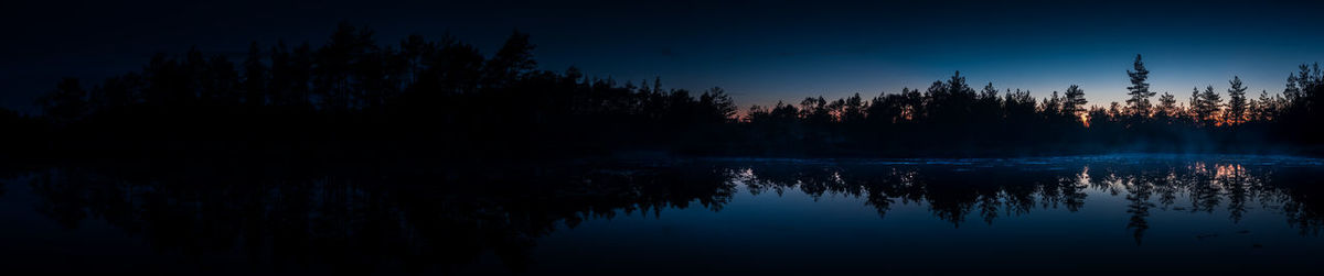 Reflection of silhouette trees in lake against sky at night