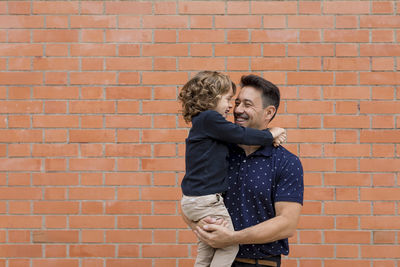 Happy father carrying son at brick wall