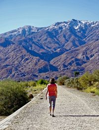 Rear view of woman walking on road against mountain range