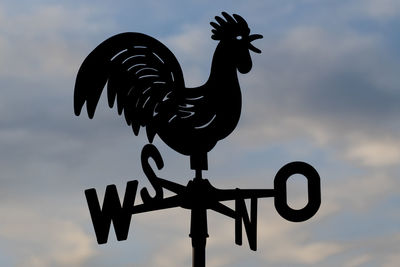 Low angle view of weather vane against cloudy sky