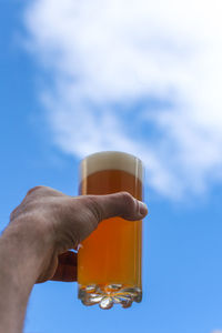 Close-up of hand holding beer glass against sky