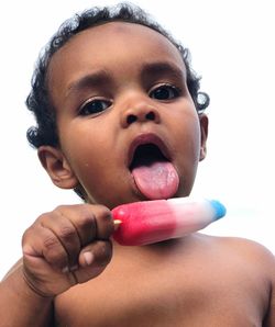 Close-up portrait of shirtless boy eating popsicle against clear sky