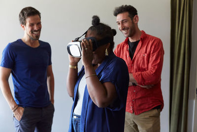 Businessmen smiling while looking at female colleague using virtual reality simulator in office