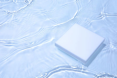 Empty white square podium on transparent clear blue water background