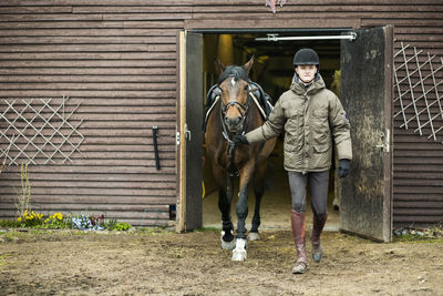 Full length of young man with horse leaving barn