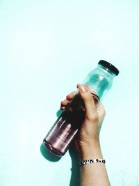 Close-up of hand holding glass bottle against white background