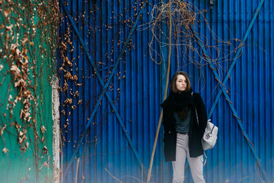 Portrait of young woman standing against blue wall