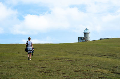 Rear view of woman walking on field against sky