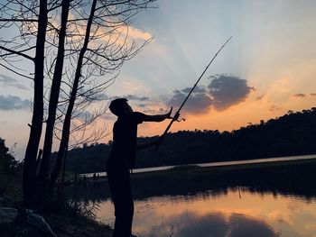 Silhouette man fishing by lake against sky during sunset