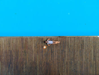 Woman sitting on wood against blue color of the swimming pool 