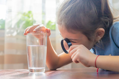 Girl looking at water through magnifying glass at home