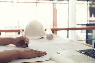 Cropped hands of male architect drawing blueprint at desk in office