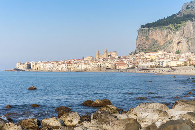 Buildings by sea against clear blue sky