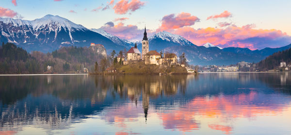 Scenic view of lake by buildings against sky during sunset