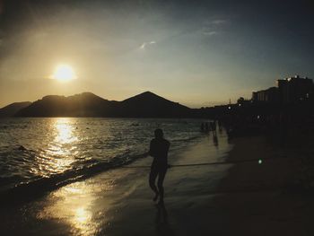 Silhouette man standing on beach against sky during sunset