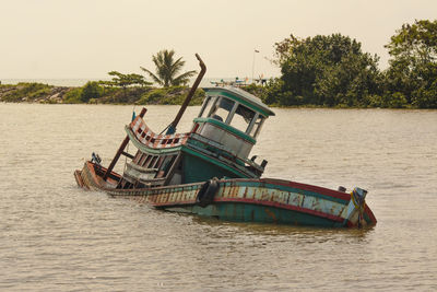 The boat is sinking in the river with clear sky.