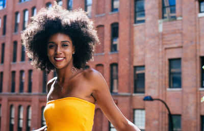 Portrait of happy young woman with afro hairstyle standing on bridge against building