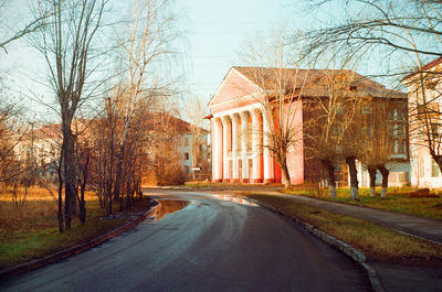 Empty road along trees and buildings