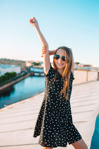 Young woman wearing sunglasses standing against sky