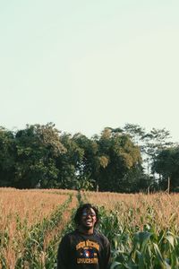 Portrait of smiling young woman standing on field against clear sky