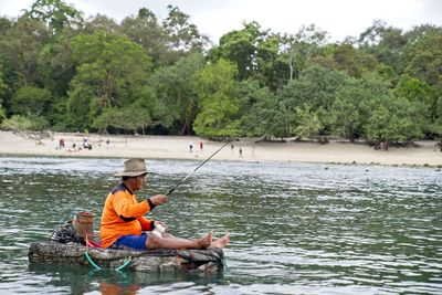 Man fishing in river against trees