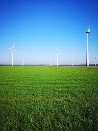 Wind turbines on field against clear blue sky