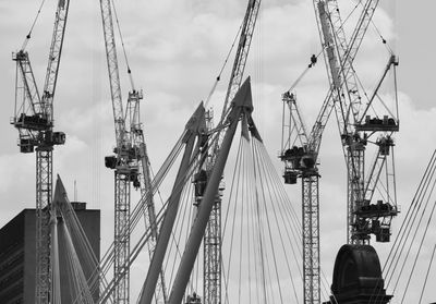 Low angle view of cranes against cloudy sky