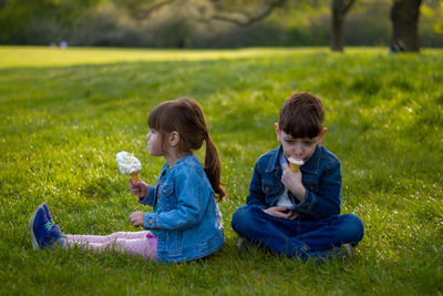 Boys and girl sitting on grassy field eating ice cream