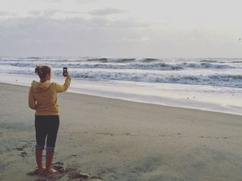 Rear view of woman photographing on beach