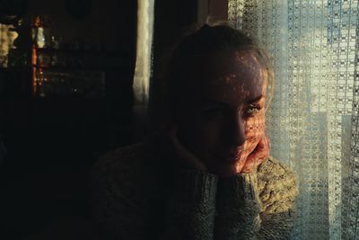 Close-up of young woman looking away by window with shadow