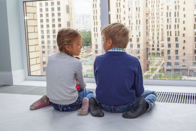 Rear view of friends sitting on window