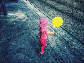 Full length of girl with yellow balloon walking on sidewalk