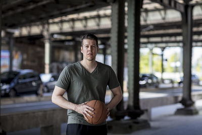 Portrait of young man with basketball standing on bridge