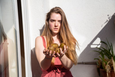 Portrait of young woman holding kiwis against wall