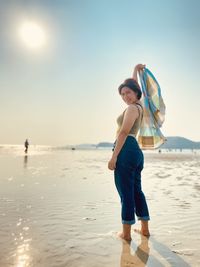 Woman holding umbrella on beach against sky