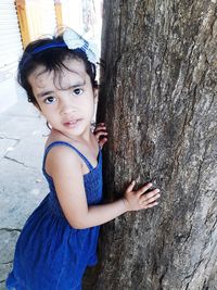 Portrait of cute girl standing by tree trunk